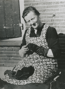 876862 Portret van een onbekende vrouw die sokken aan het stoppen is, zittend aan een onbekende straat in Wijk C te Utrecht.